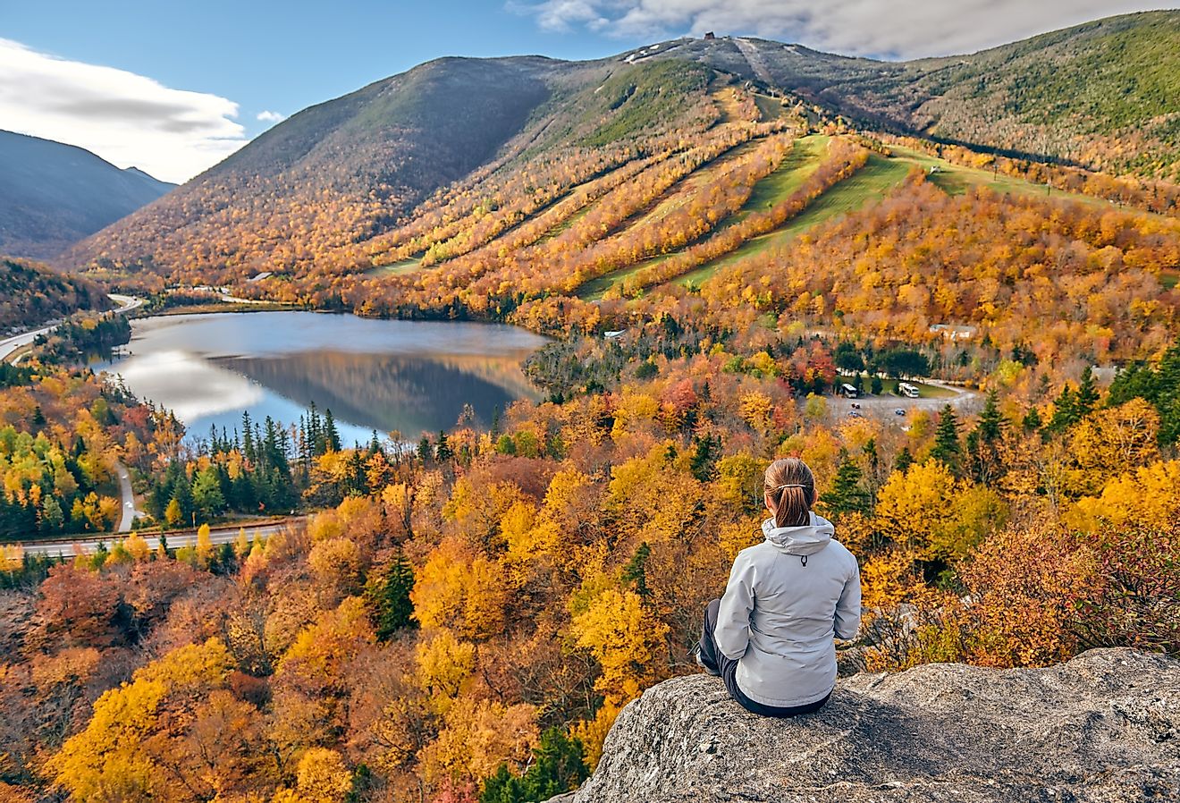 Woman hiking at Artist's Bluff in autumn, with a view of Echo Lake, New Hampshire.