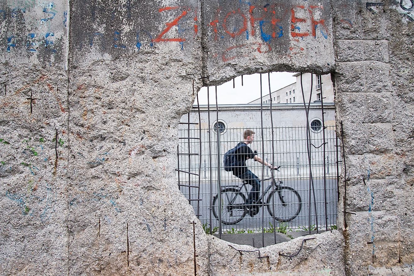 A man ride a bicycle pass the hole in section of ruined Berlin Wall in Germany.