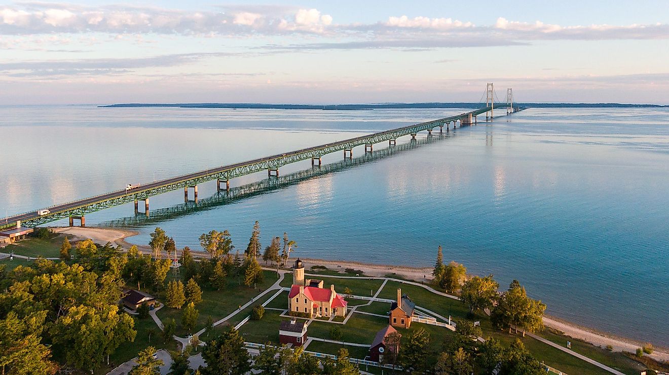 Aerial view of the Mackinac Bridge over calm waters in the morning, with view of the Old Mackinac Lighthouse