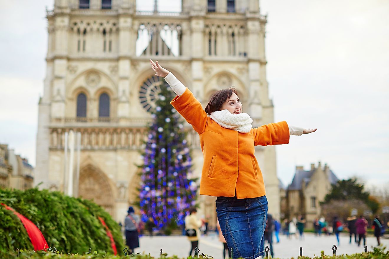 Happy young tourist in Paris on a winter day with main Parisian Christmas tree and Notre-Dame cathedral in the background. Image credit: Ekaterina Pokrovsky/Shutterstock.com
