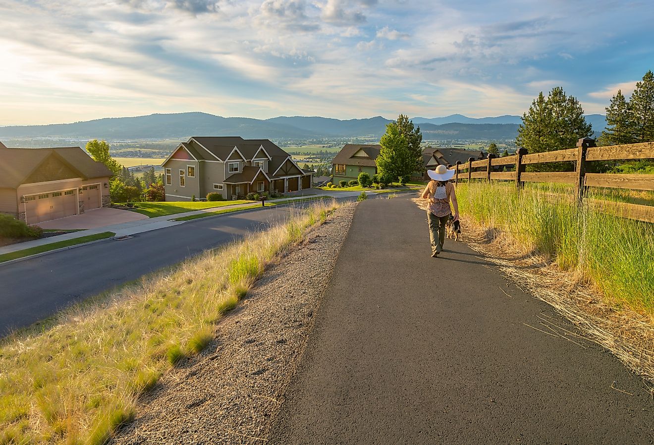 A woman with a hat walks her dog on a paved hillside walking trail in the community of Liberty Lake, Washington. Image credit Kirk Fisher via Shutterstock