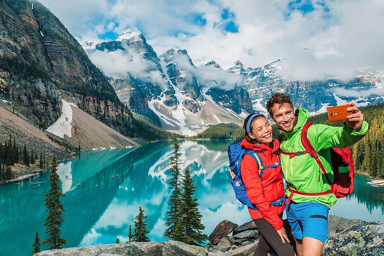 Young hikers taking a selfie on a Canada travel hike at Moraine Lake. Couple tourists using phone to capture memories on their Banff holiday.