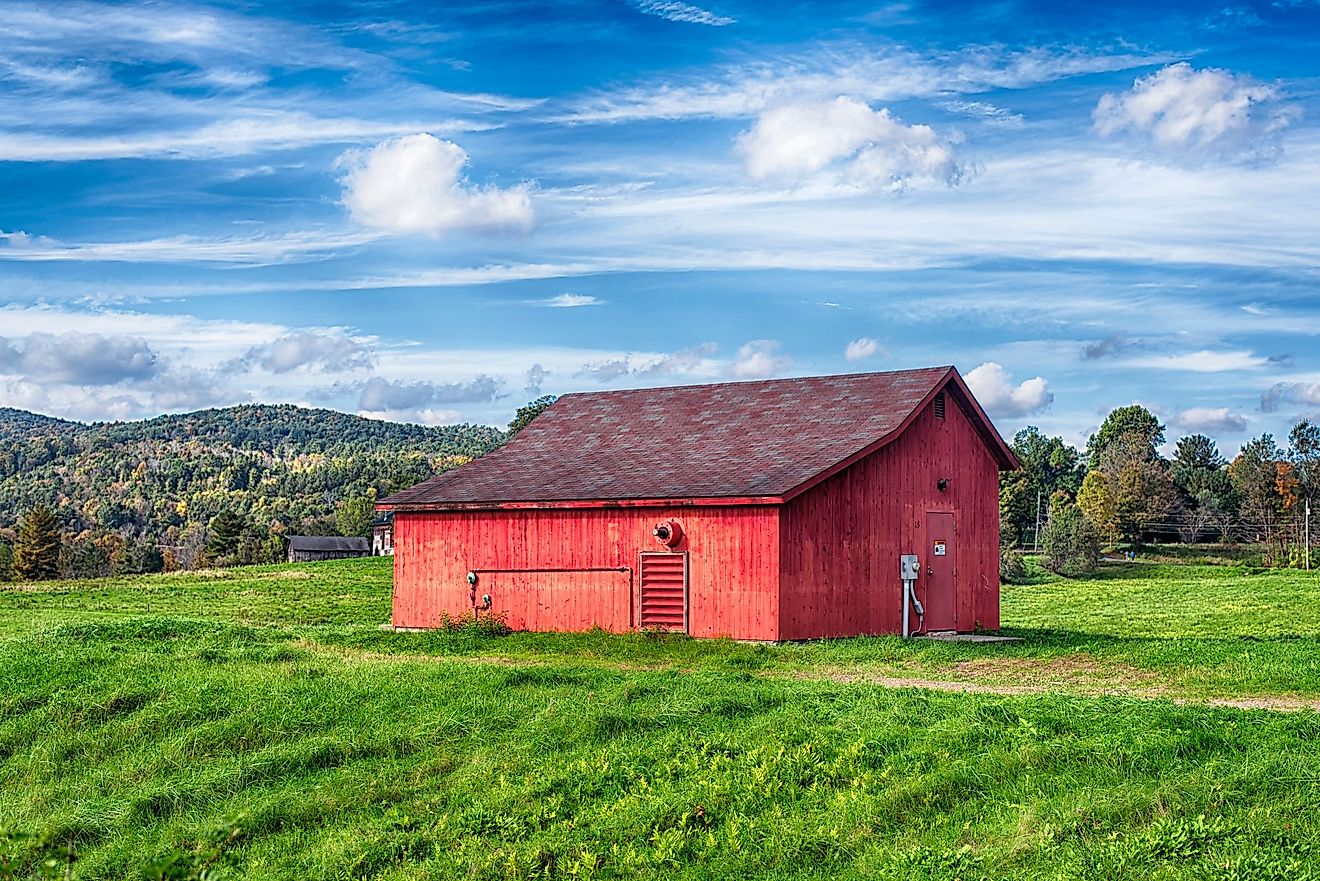A red barn on a field landscape in the New England town of Cornwall, Connecticut on a blue sky day. 