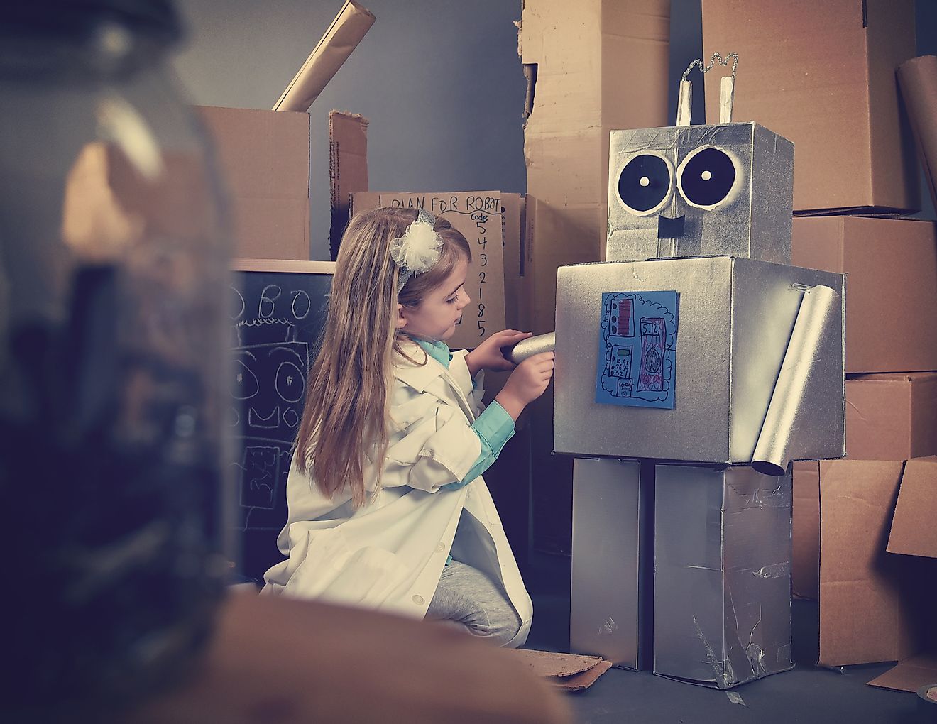 A science student is inventing a metal robot out of cardboard boxes with tools.