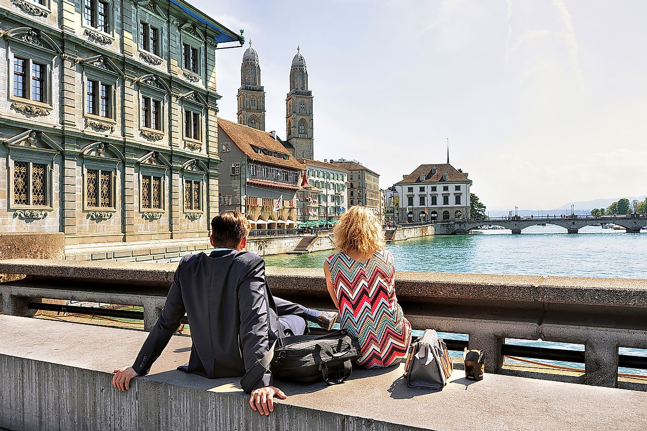 A Swiss couple sitting at Limmat River Quay and looking at Grossmunster Church in Zurich, Switzerland. Image credit: Roman Babakin/Shutterstock.com