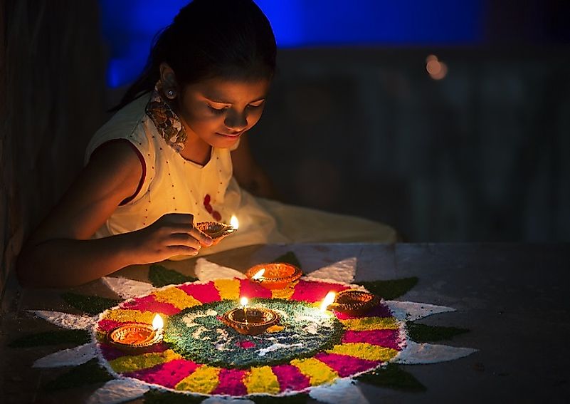 A young Hindu girl arranges oil lamps and decorates rangolis during Diwali.