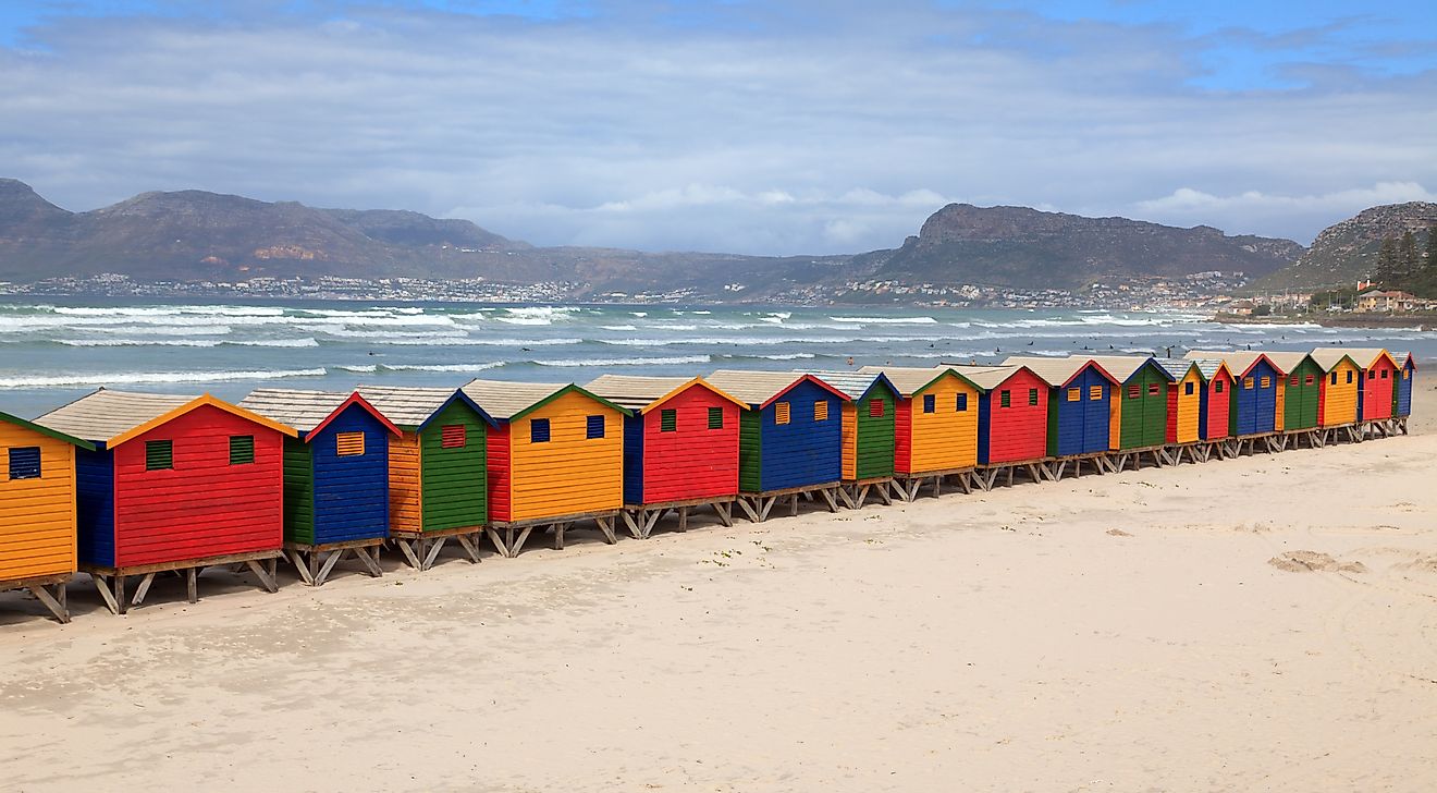 Muizenberg is famous for its rows of colorful beachside huts, with surfers in the background. The area is one of the most popular surfing venues in South Africa.