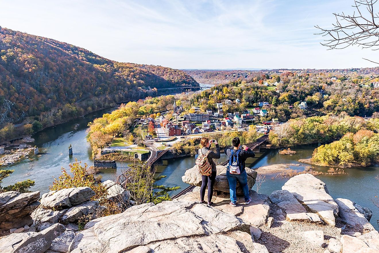 Overlook with hiker couple, colorful orange and yellow foliage in the fall autumn forest, with a small village town by the river in Harper's Ferry, West Virginia, USA. Editorial credit: Andriy Blokhin / Shutterstock.com