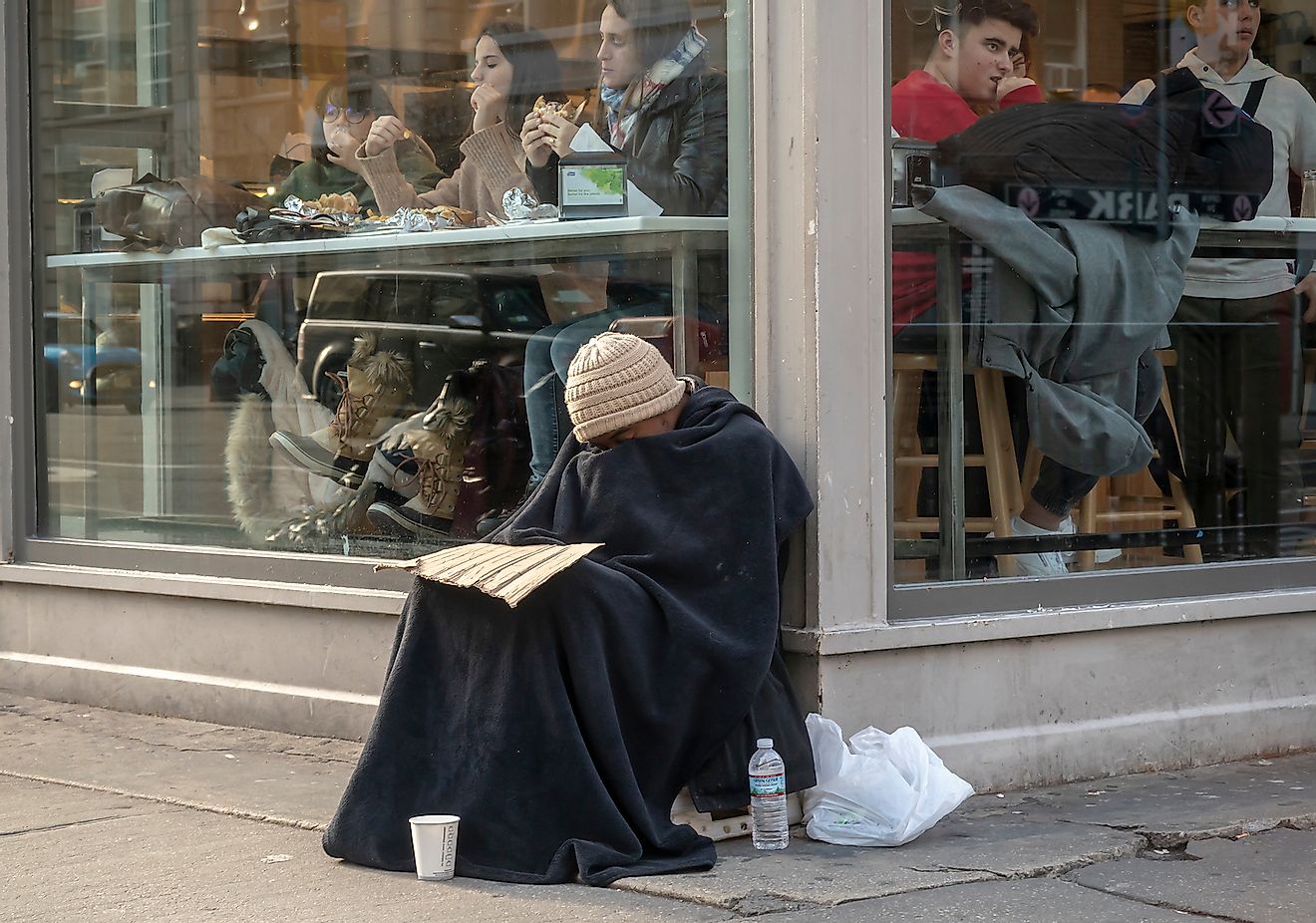 Homeless individual begs in front of a restaurant in the Chelsea neighborhood of New York. Image credit: Rblfmr/Shutterstock.com