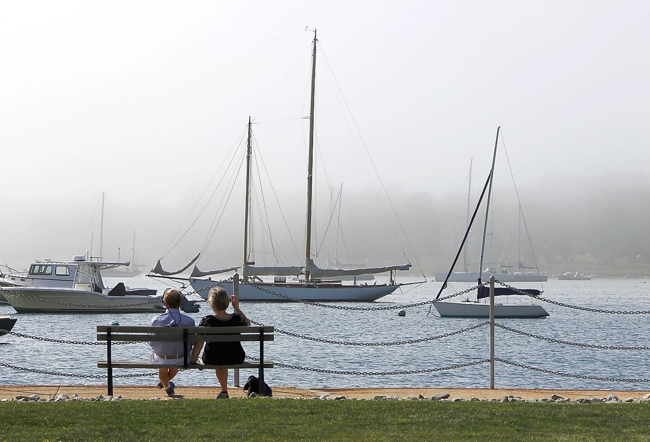 Couple on a bench looks out over a foggy harbor full of boats in Stonington. Image credit: TheBrassGlass via Shutterstock.