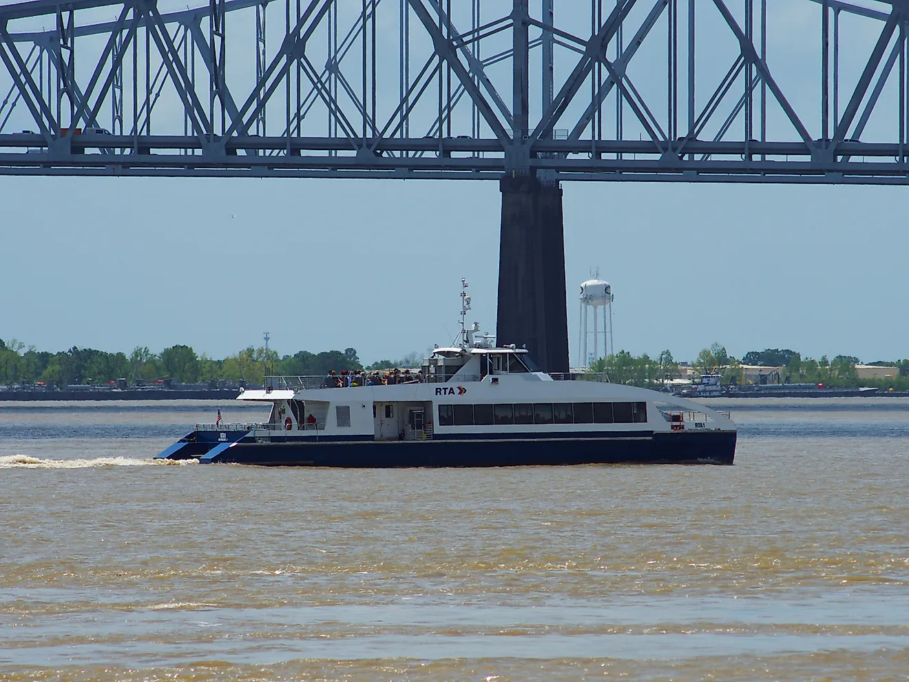A ferry crosses the Mississippi River under a bridge in New Orleans, via Wirestock on iStock.com