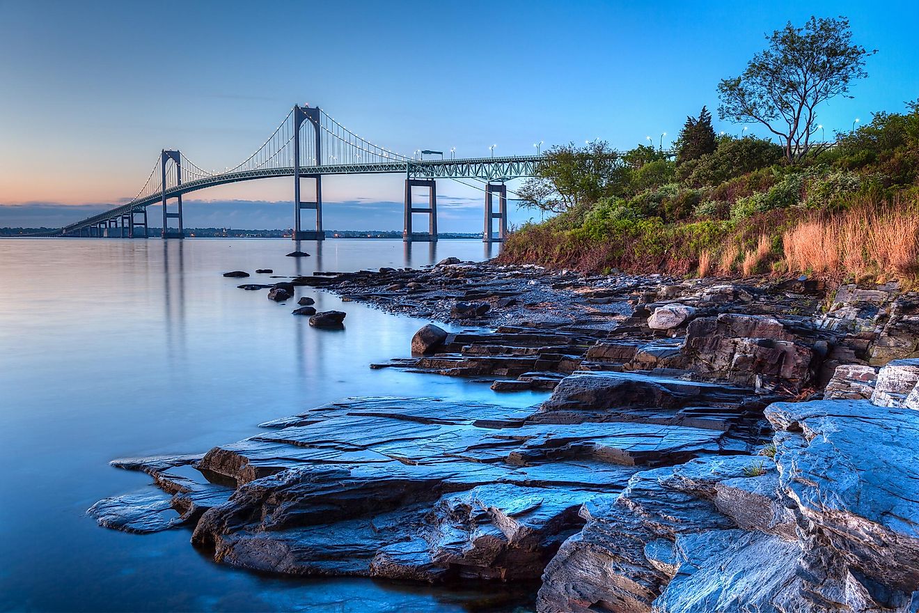 Long exposure HDR of the illuminated Newport Bridge from Taylor's Point near Jamestown, Rhode Island, USA, with a rocky seascape in the foreground at sunrise.