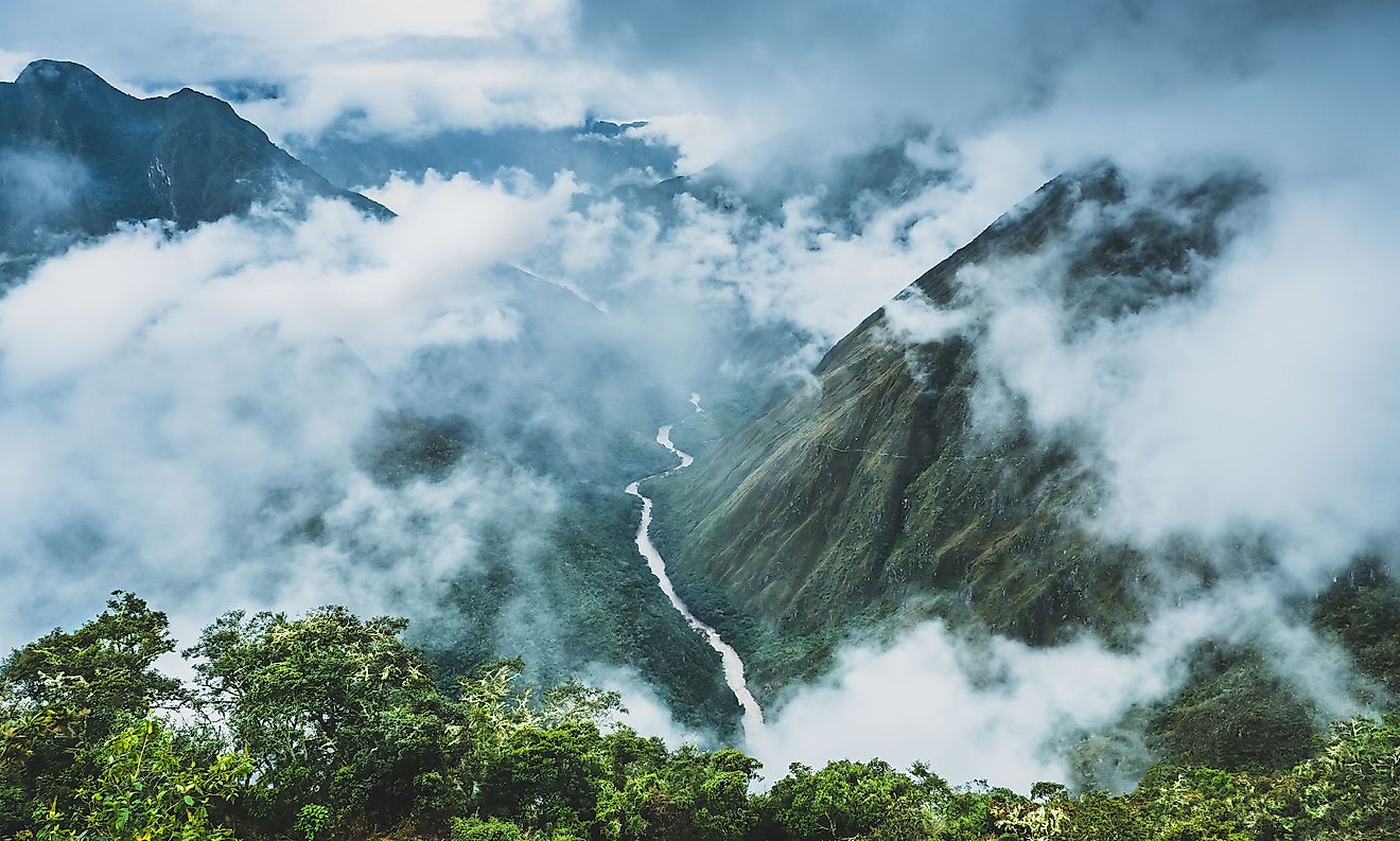 Looking down from Phuyupatamarca on the Inca Trail, into a cloud forest where a silver river winds through the lush green jungle and clouds.