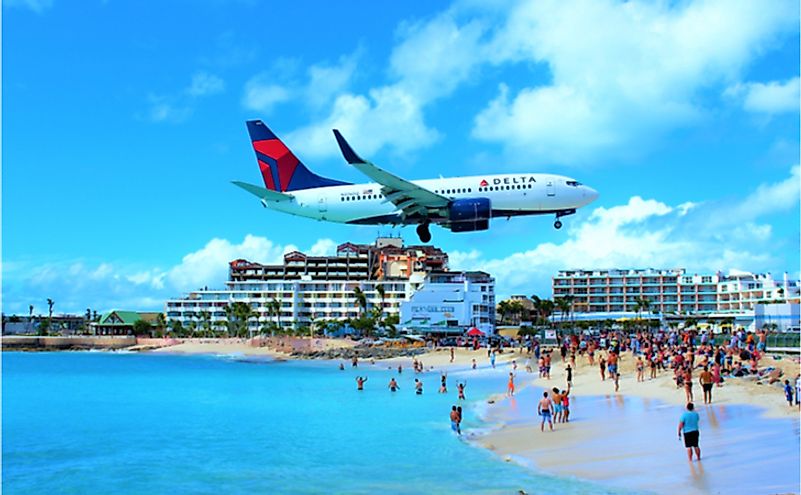 A Delta Air Lines passenger jet flying over Maho bay as it comes in to land at SXM Princess Juliana International Airport behind. 