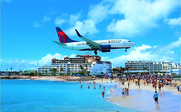 A Delta Air Lines passenger jet flying over Maho bay as it comes in to land at SXM Princess Juliana International Airport behind. 