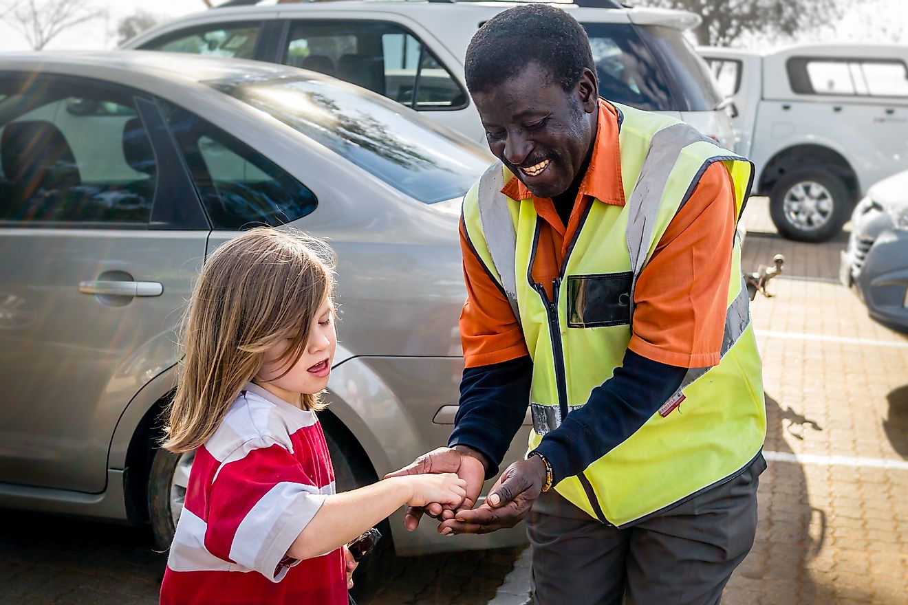 A young girl tips a friendly black security car park attendant. Image credit: HASPhotos/Shutterstock.com