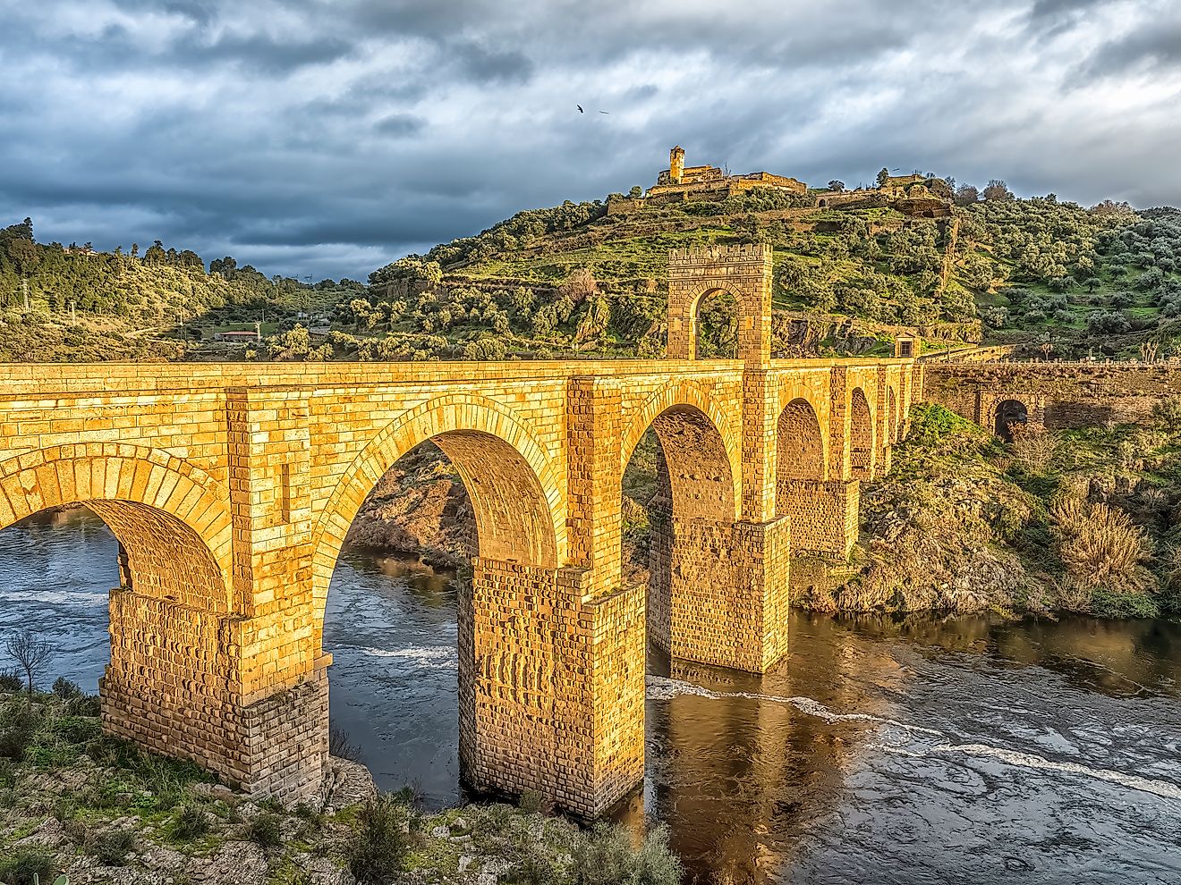 Ancient Roman stone arch bridge connecting hills over Tagus River in Alcántara, Spain.