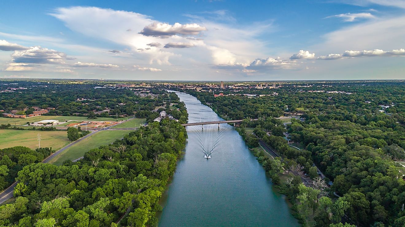 A boat sails down the Brazos River with the skyline of Waco, Texas sitting behind. 