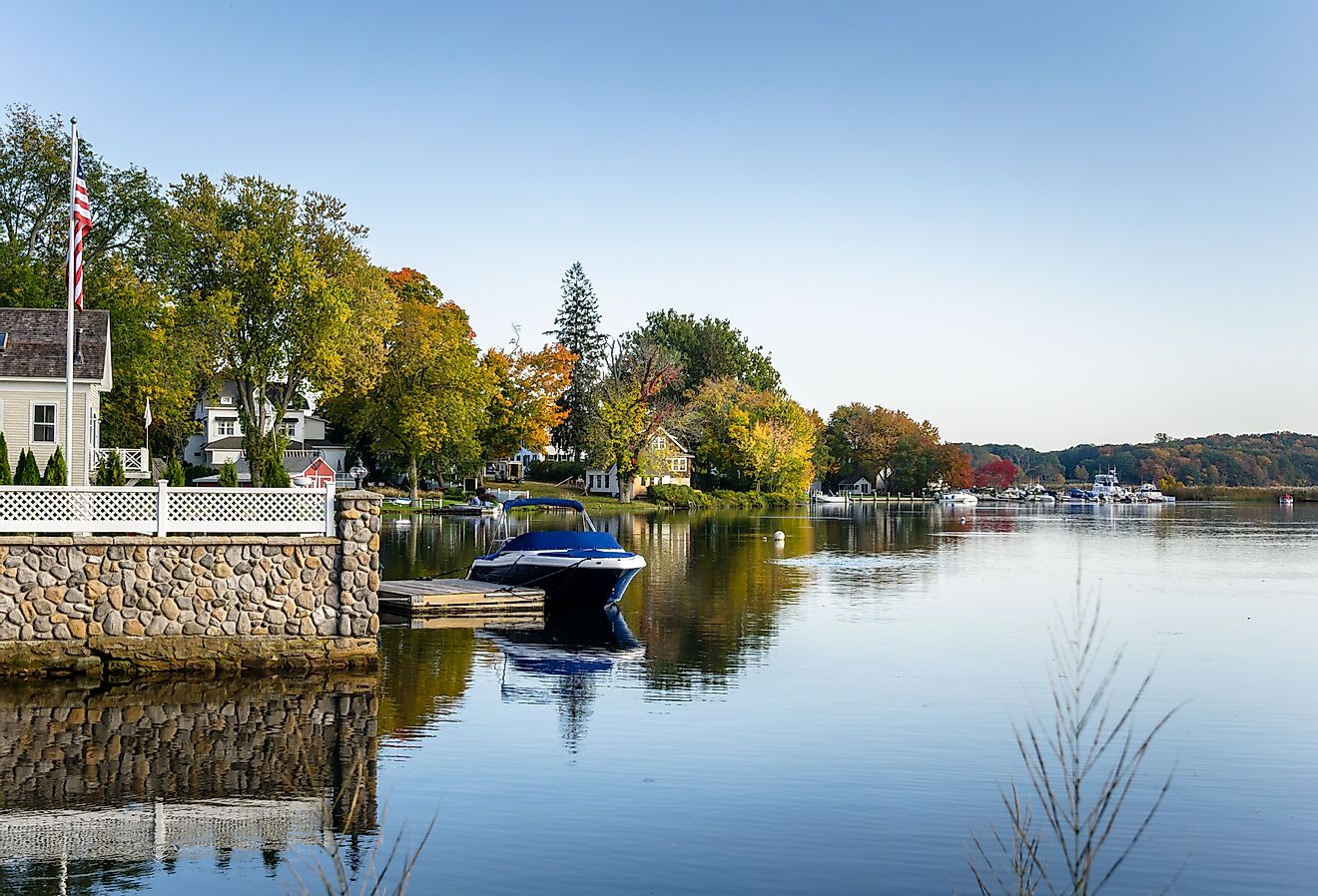 Waterside houses among trees with boats moored to wooden jetties on a clear autumn day, Connecticut River, Essex.