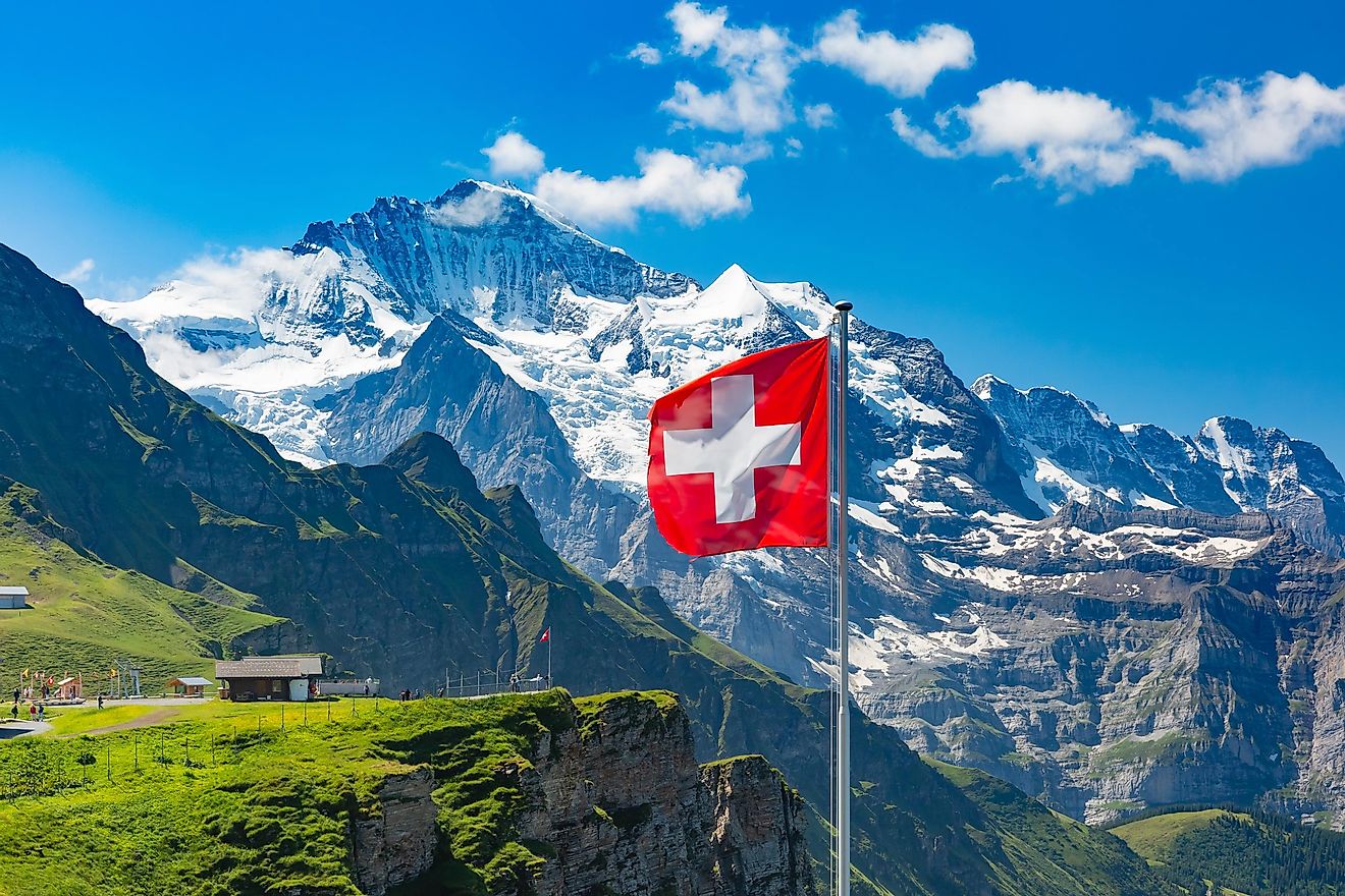 Swiss flag waving and tourists admire the peaks of Monch and Jungfrau mountains on a Mannlichen viewpoint, Bernese Oberland Switzerland