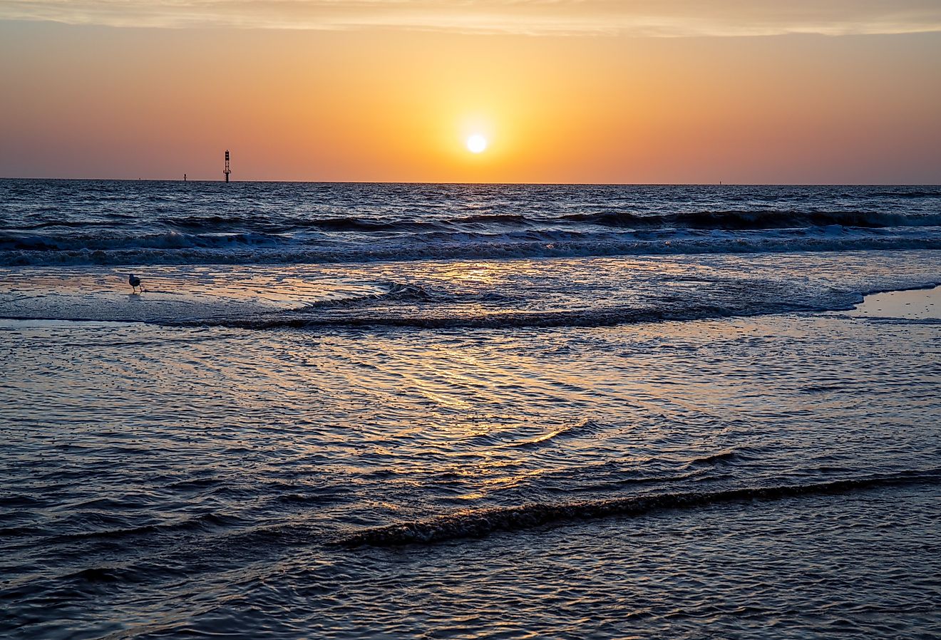 Sunset with warm glow and reflection of sun on calm Gulf waters in Seaside, Florida.