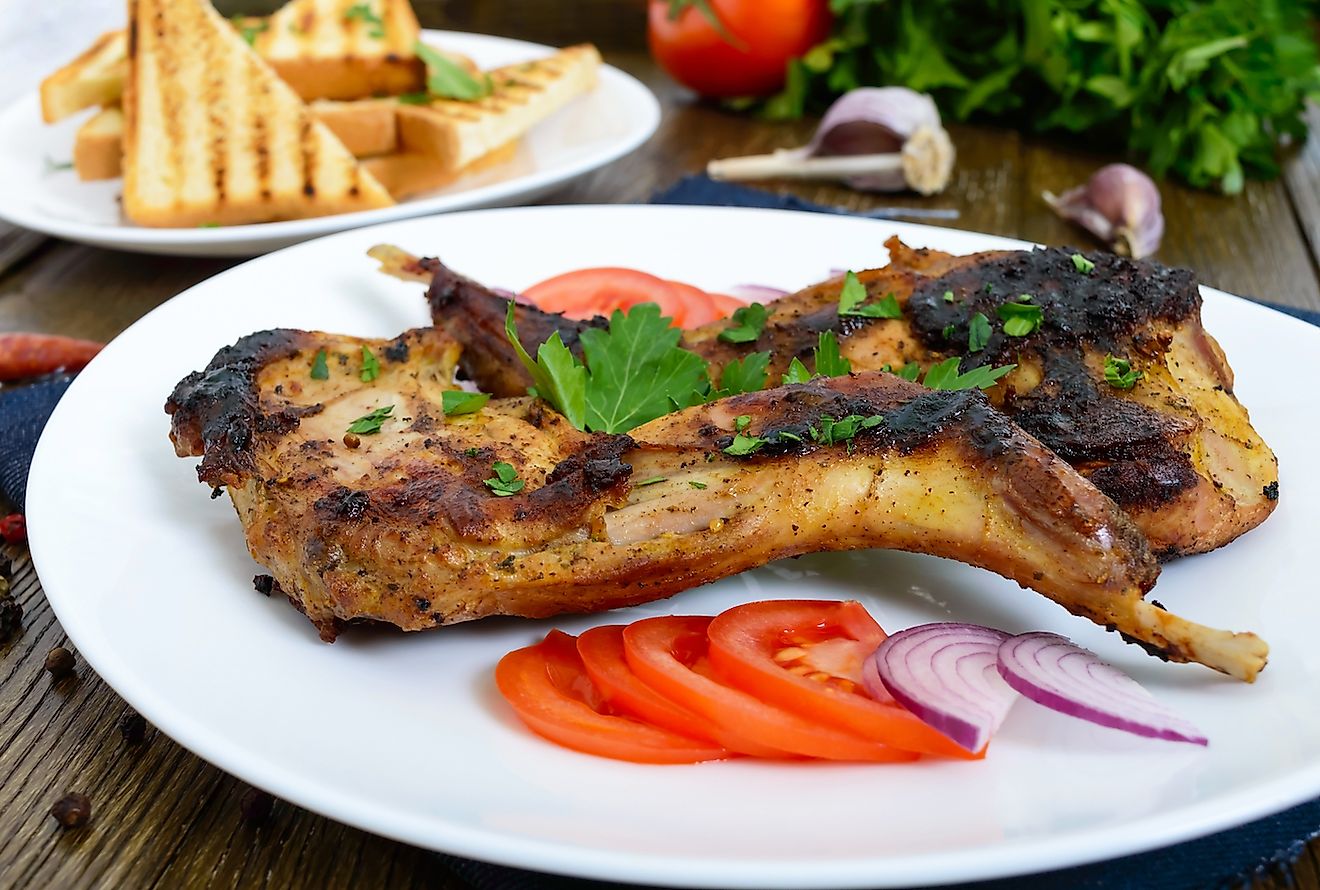 Fried rabbit legs on a white plate on a wooden table. Image credit: Iaroshenko Maryna