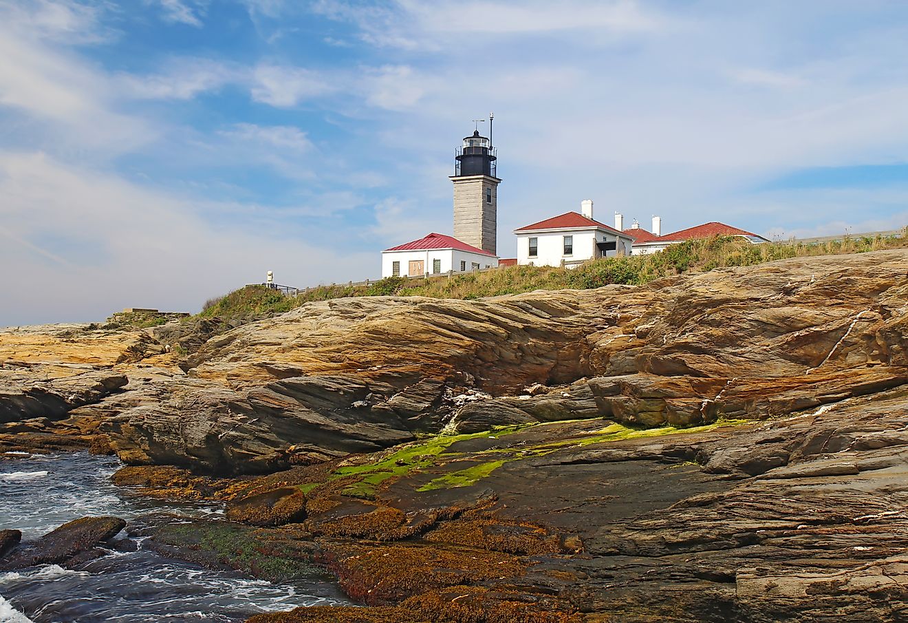 Editorial Photo Credit:Stephen B. Goodwin via Shutterstock. The Beavertail Light lighthouse near Jamestown on Conanicut Island, Rhode Island, viewed from the rocky coast with a bright blue sky and white clouds