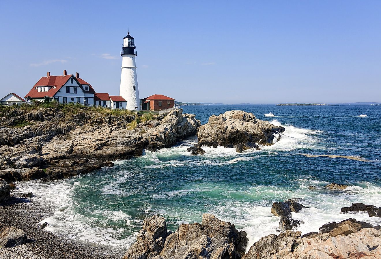 Lighthouse in Portland, Maine and waves crashing on the rocky shore.