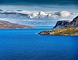 The remote Bering Strait near Alaska features cold deep blue water, rugged northern mountains, dramatic clouds and pristine Arctic wilderness.