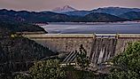 A picture of Shasta Dam with a lake and rocky mountains on the background during sunset. 
