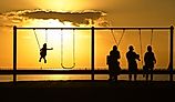 Mandeville, Louisiana: Families in silhouette play on the swings overlooking Lake Pontchartrain at sunset