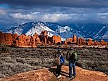 Couple enjoying beautiful mountain view on hiking trip in Utah. The Windows Section of the park, snow covered La Sal Mountains in the background. Arches National Park ,Moab, Utah.