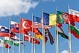 A group of flags from countries from around the world on flagpoles, fluttering in the wind against the backdrop of a blue sky.