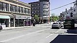 Traffic and pedestrians moving past storefronts along a sunny urban street in Port Chester, New York. 