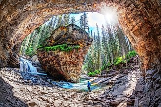 Hiker stands in awe of waterfall and limestone bedrock at a hidden cave in Johnston Canyon at Banff National Park.