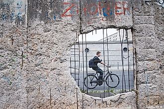 A man ride a bicycle pass the hole in section of ruined Berlin Wall in Germany.