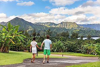 Couple tourists walking on Hawaii vacation. Two young people relaxing in Hanalei Bay resort in Kauai, Hawaii travel beach destination with Kauai mountains in the background.
