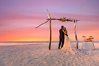 Bride and groom on the beach under wedding arch with cake.