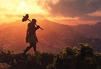 Primitive man walking on the grass with the sun setting.