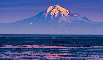 Mount Redoubt is illuminated by the rising sun as it stands tall over the calm waters of Cook Inlet.