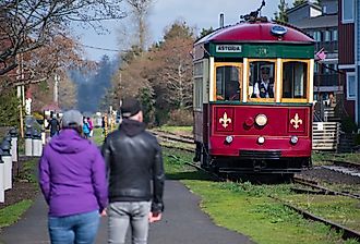 A couple walks along the Astoria Riverwalk as the Astoria Riverfront Trolley passes by. Image credit: Charles-McClintock Wilson via Shutterstock.