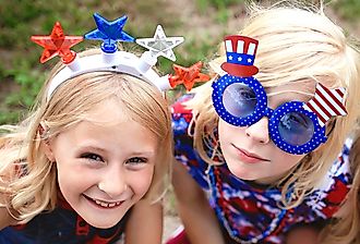 Two Patriotic little kids are sitting at a Fourth of July parade in a small town in America.