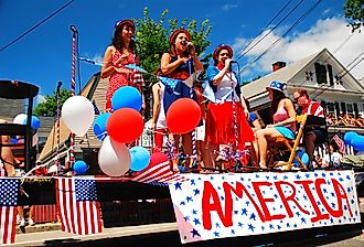 Three teenage girls sing patriotic tunes while traveling on a float during a Fourth of July parade in Bristol, Rhode Island. Image credit James Kirkikis via Shutterstock