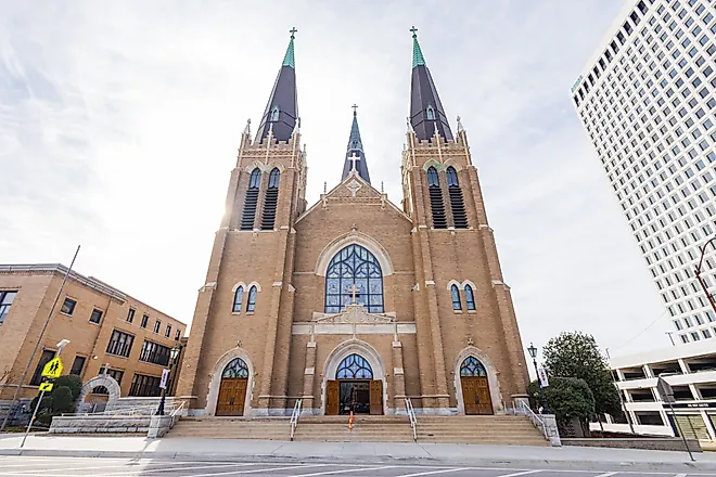 Exterior of Holy Family Cathedral in Tulsa, featuring Romanesque Revival architecture with arched windows, twin bell towers, and a detailed brick facade
