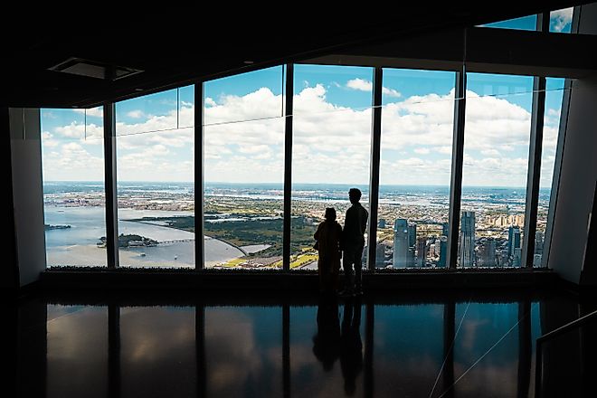 Couple standing in front of the large glass windows at One World Observatory, overlooking the New York City