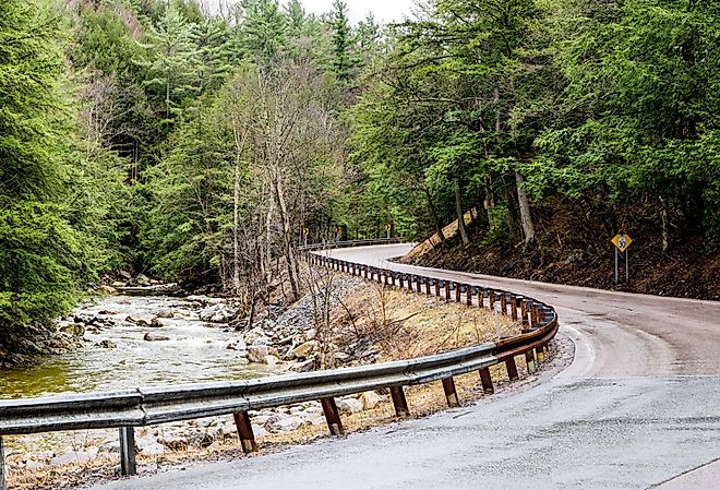 A narrow road curves beside a rushing stream at the eastern edge of the Adirondack Mountains in northeast New York.