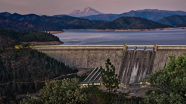 A picture of Shasta Dam with a lake and rocky mountains on the background during sunset. 
