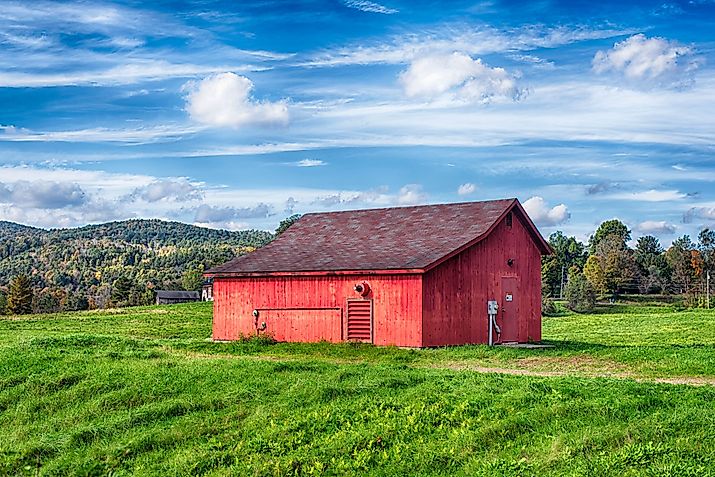 A red barn on a field landscape in the New England town of Cornwall, Connecticut on a blue sky day. 