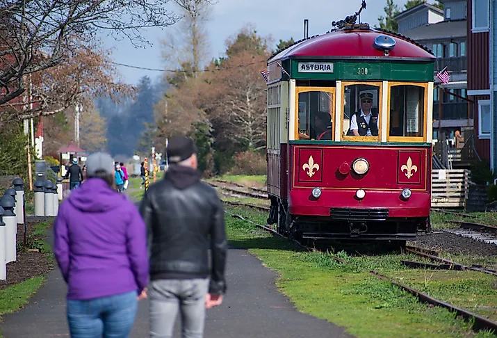 A couple walks along the Astoria Riverwalk as the Astoria Riverfront Trolley passes by. Image credit: Charles-McClintock Wilson via Shutterstock.