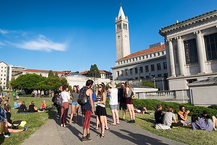 tudents at the University of California Berkeley campus enjoying a warm spring day outdoors on the grass. The Campanile tower is seen in the background.